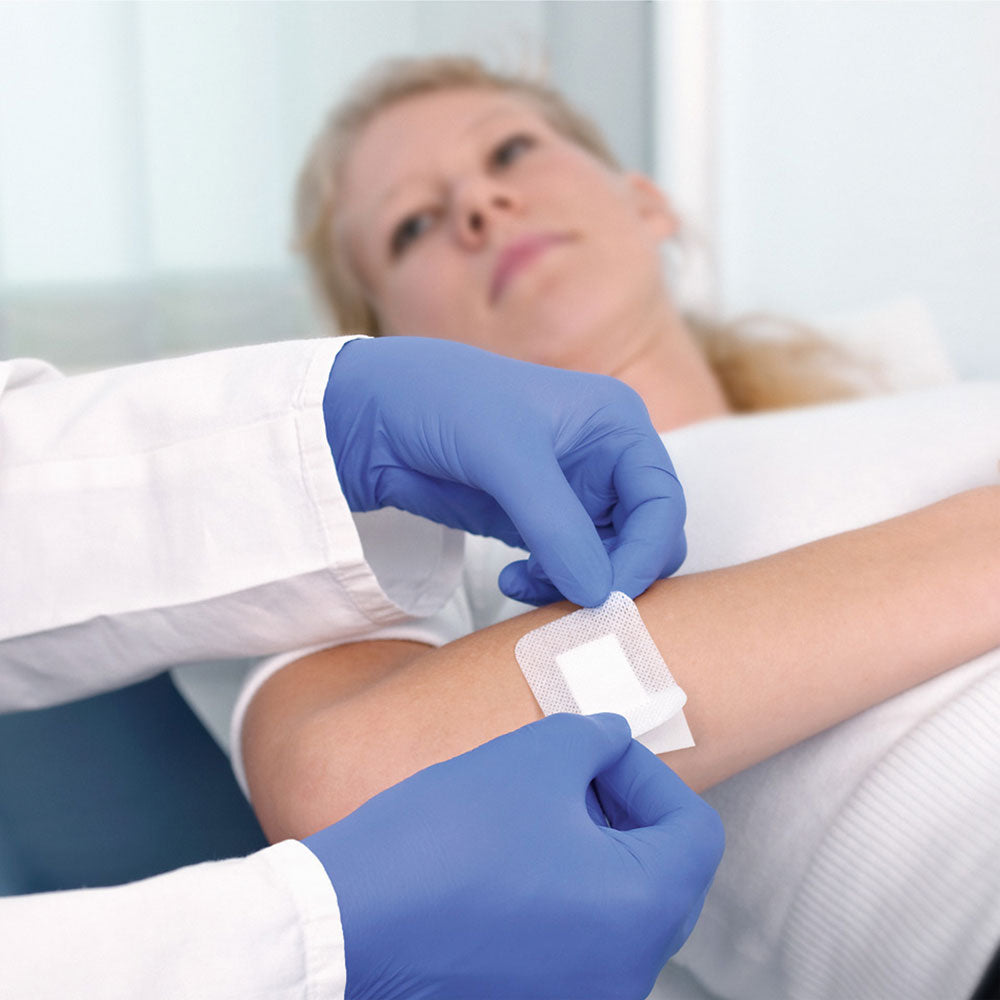 Blau behandschuhte Hand versorgt eine Patientin mit Pflaster auf dem Bein