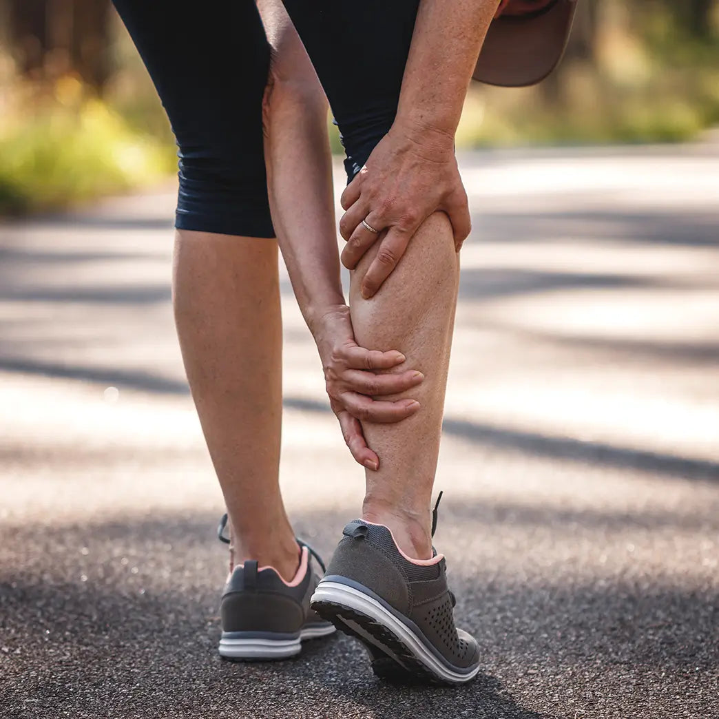 A woman in sportswear holding her leg, in need of cold spray